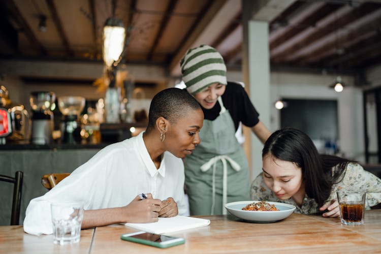 Cheerful Coworkers Tasting And Smelling Food In Restaurant