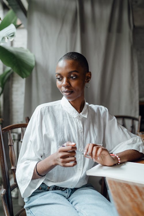 Free Pensive young bald African American female in white shirt relaxing in cafe on sunny day Stock Photo