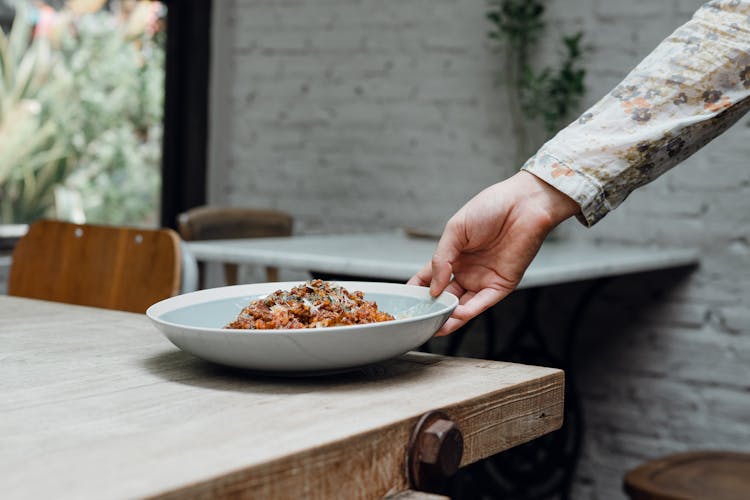 Crop Waitress Serving Plate Of Appetizing Food On Table