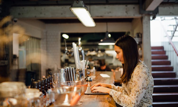 Focused Young Asian Woman Working On Laptop In Pub