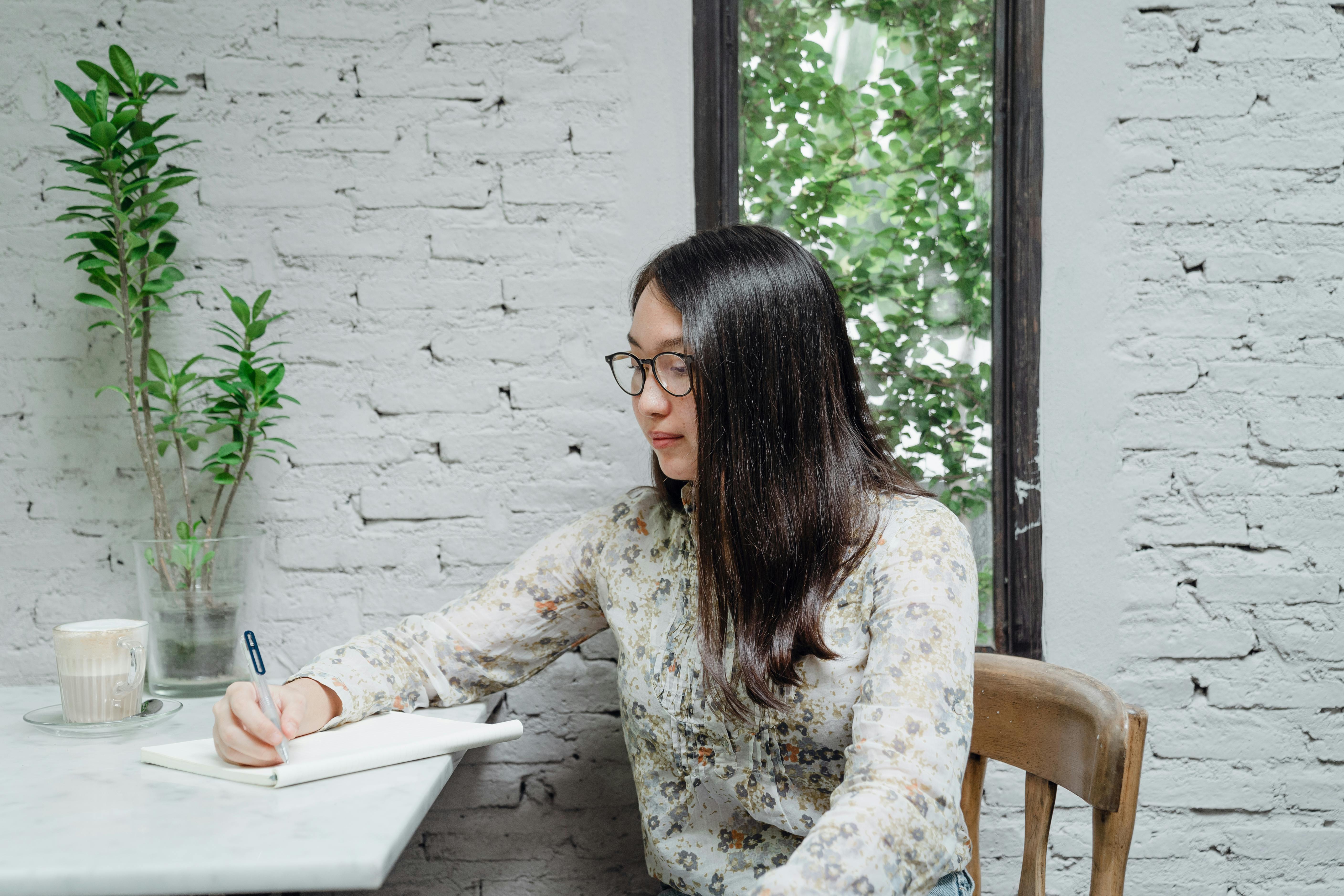 Young female Asian student taking notes in planner sitting at table ...