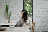 一位沉思的年轻亚洲女作家穿着休闲装，戴着眼镜，在舒适的咖啡馆里一边创作新文章，一边在日记中做笔记
