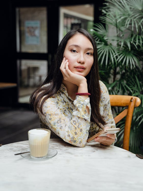 Young Asian lady with smartphone in cafe with hand at chin