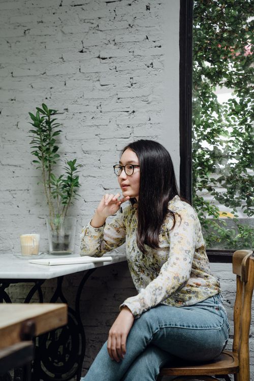 Free Focused young ethnic female entrepreneur in casual clothes and eyeglasses thinking about business ideas while working remotely in cozy cafe Stock Photo