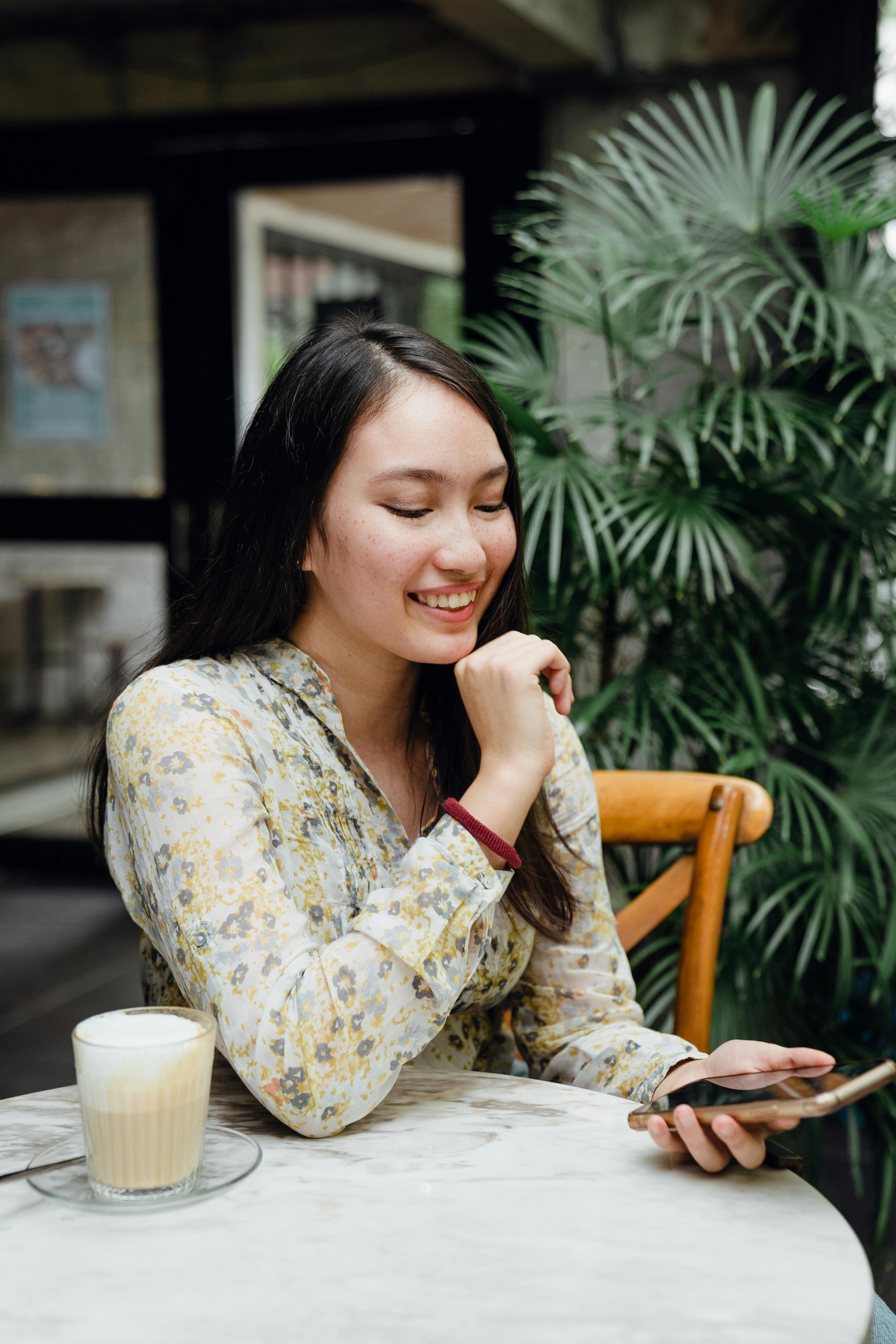 cheerful young asian woman calling on smartphone sitting in outdoor cafe