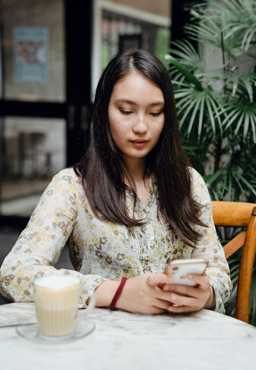 Free Young attentive Asian woman messaging on mobile phone in street cafe Stock Photo