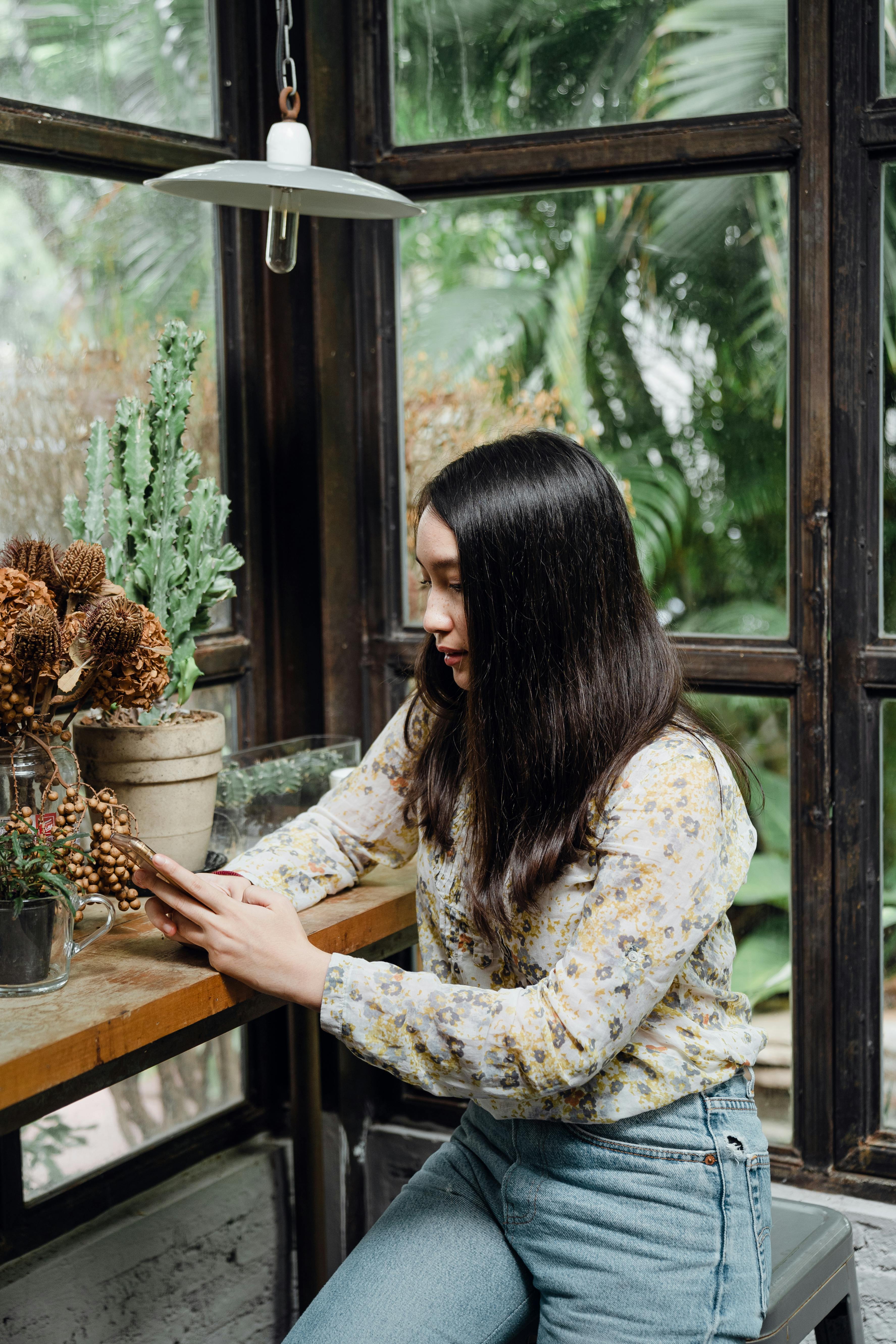 focused young asian lady texting on smartphone against window