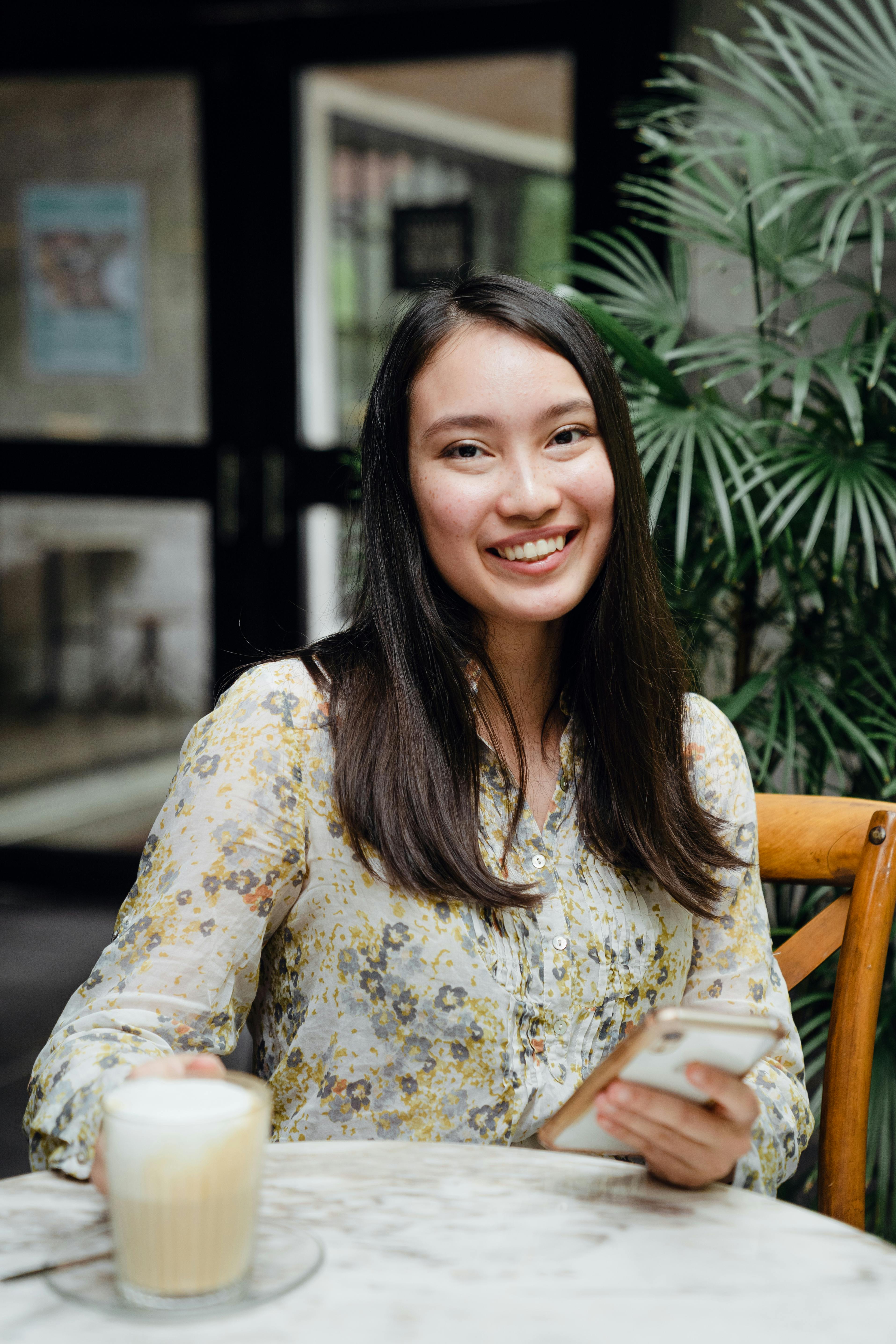 smiling young asian woman with smartphone having coffee break in street cafe