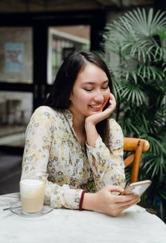 一位年轻女子在舒适的咖啡馆里，微笑着用智能手机享用咖啡