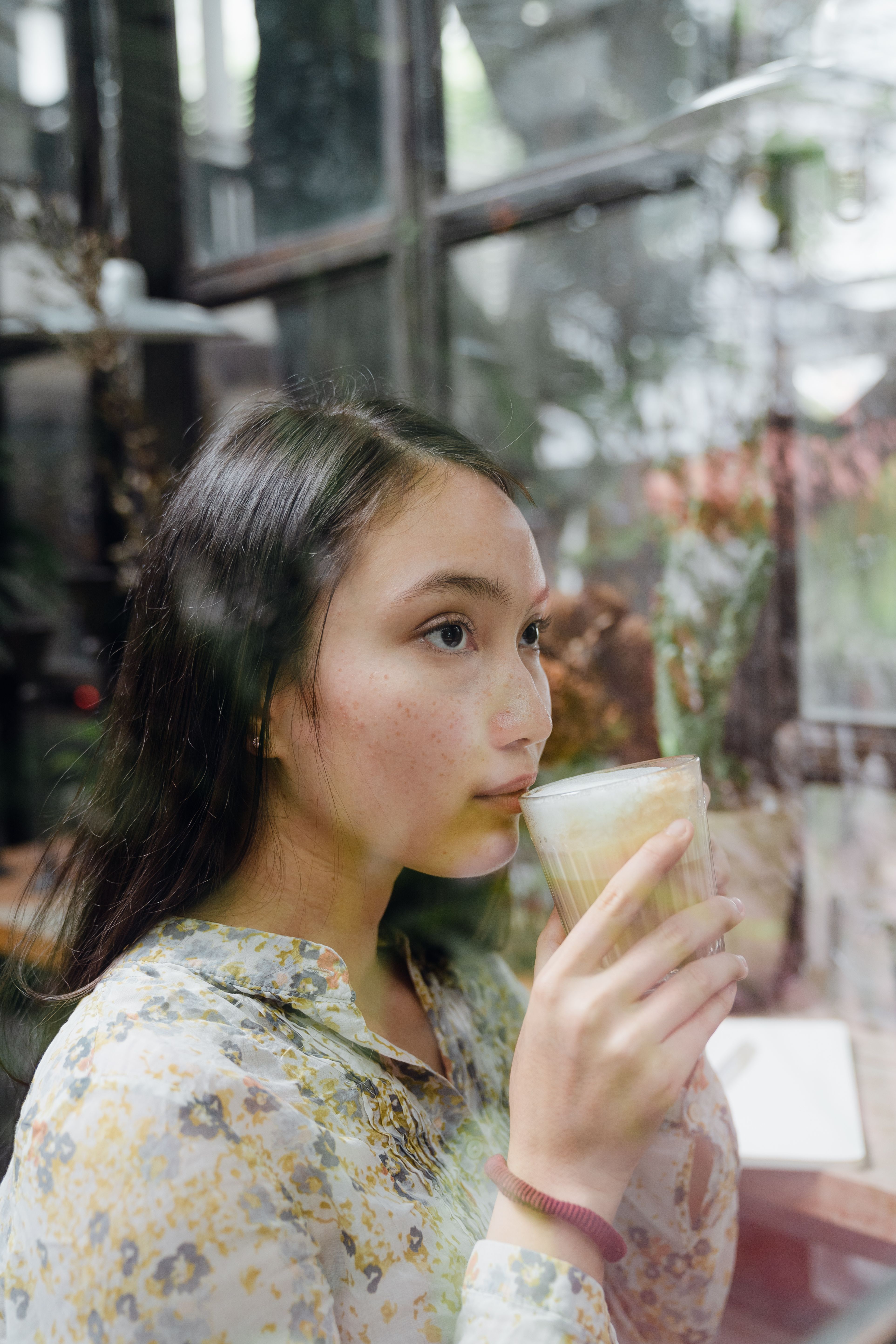 一位女士坐在一家舒适的现代咖啡馆窗边，喝着拿铁咖啡