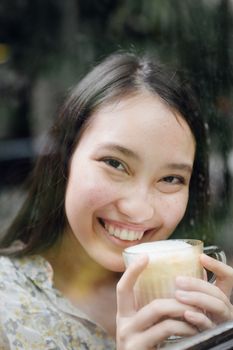 一位迷人的年轻女子，脸上带着温暖的微笑，正在一家舒适的咖啡馆里喝着拿铁咖啡
