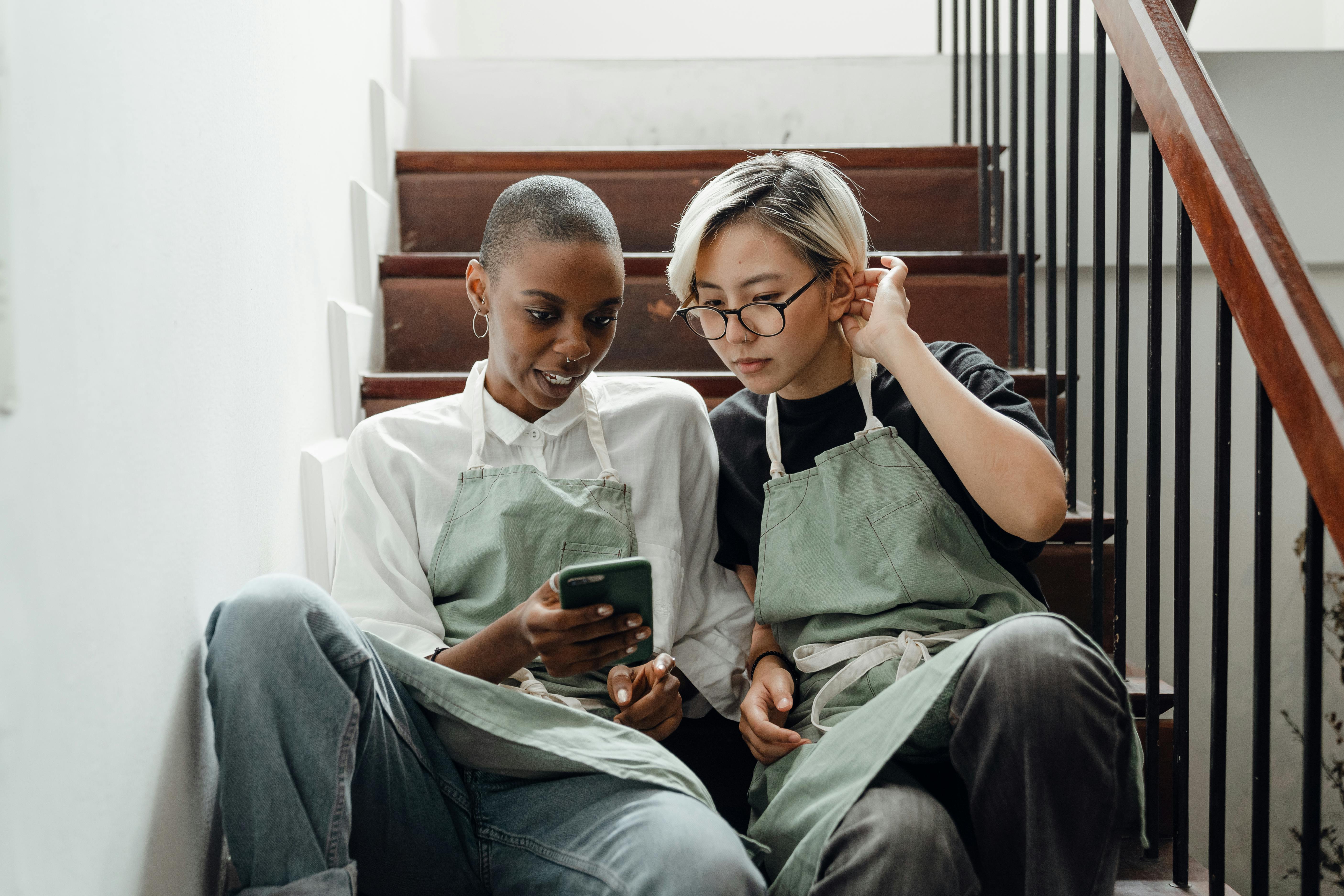 positive colleagues in aprons browsing smartphone on staircase