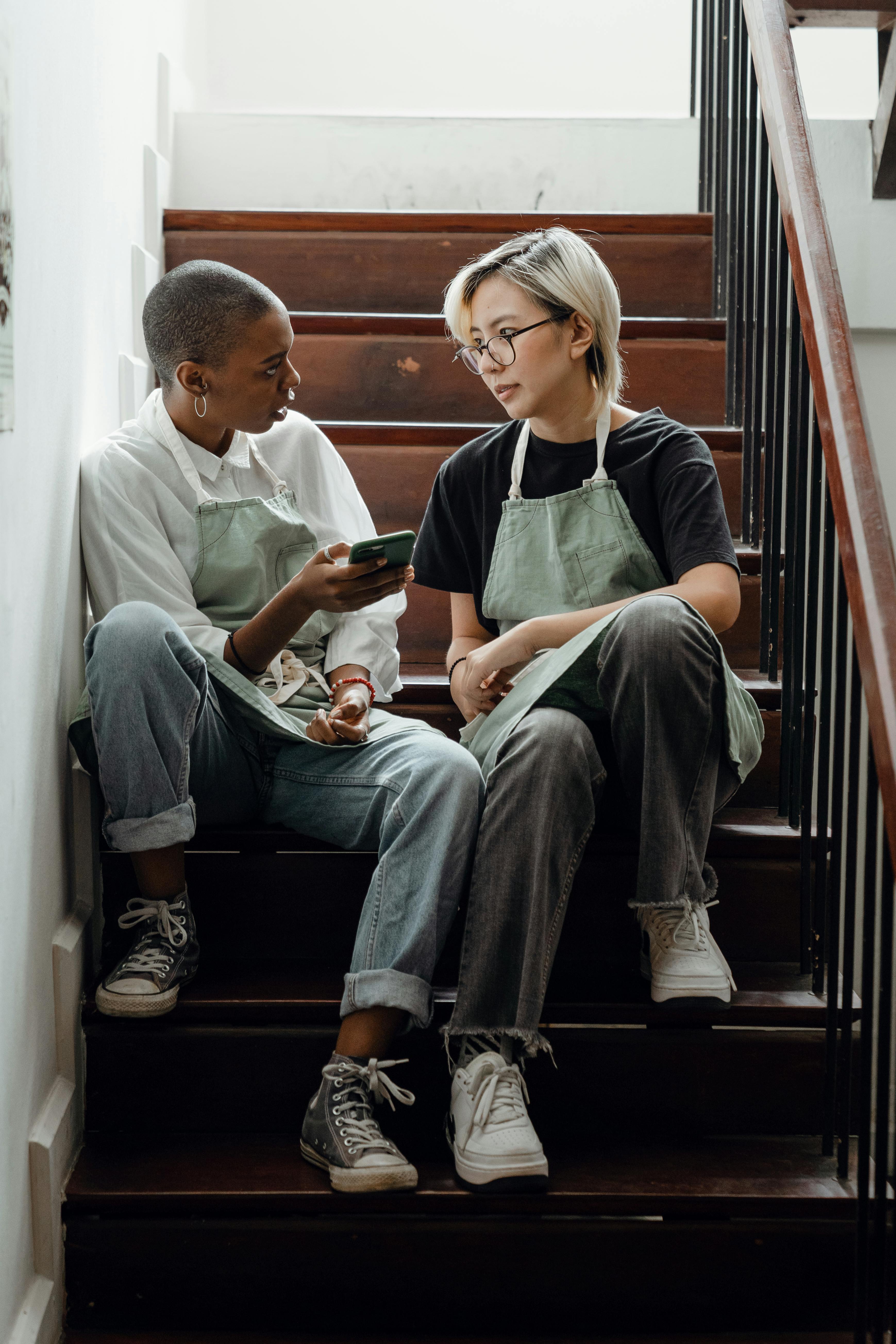 unhappy waitresses sitting on staircase with smartphone and talking