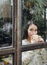 雨天，一位亚洲女性喝着咖啡，若有所思地望向窗外，营造出一种平静轻松的氛围