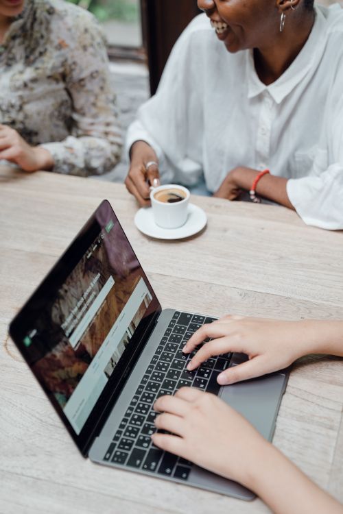 Free From above of crop anonymous female freelancer typing on laptop keyboard while sitting at table with diverse friends drinking coffee Stock Photo