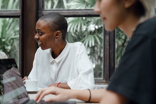 Optimistic young diverse female colleagues working on laptop and drinking coffee