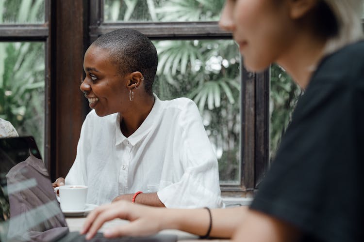 Optimistic Young Diverse Female Colleagues Working On Laptop And Drinking Coffee