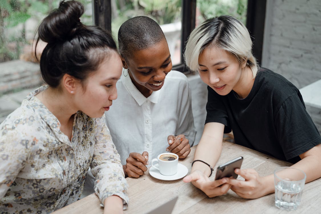 Free From above of young multiracial female colleagues discussing project and using smartphone in creative coworking space Stock Photo