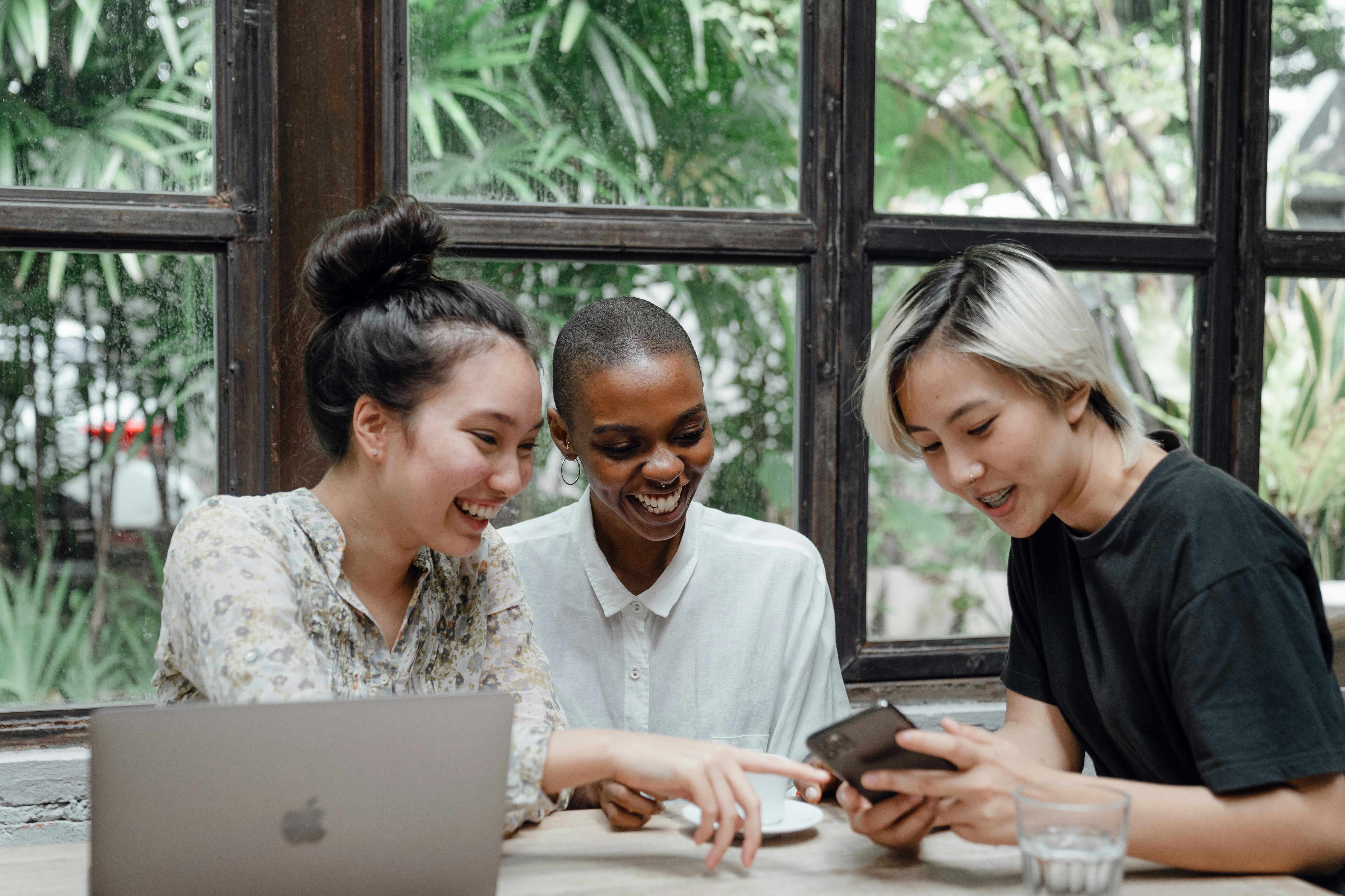 happy multiethnic women having fun while using gadgets in cafeteria