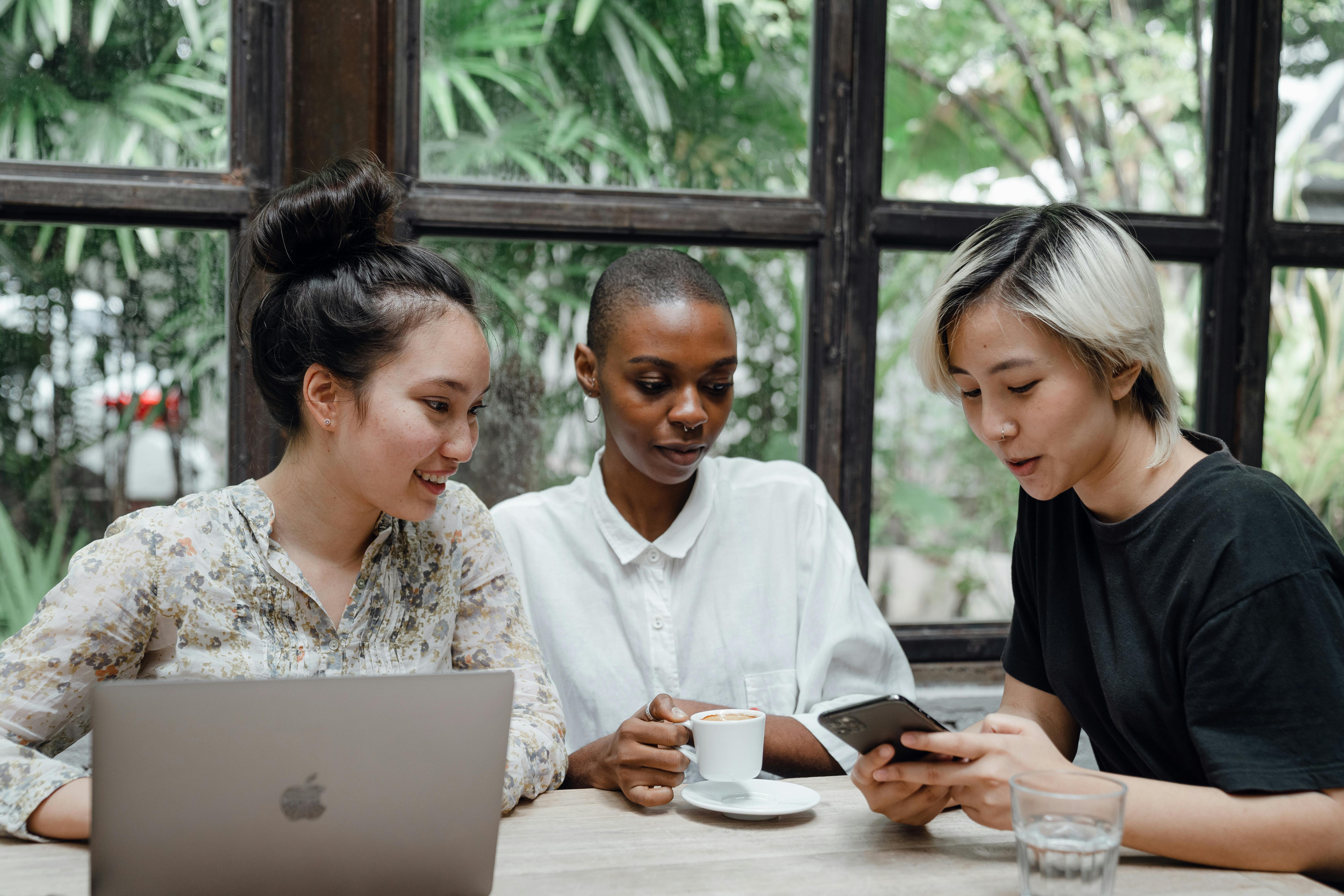 young female friends using mobile and laptop in modern cafe