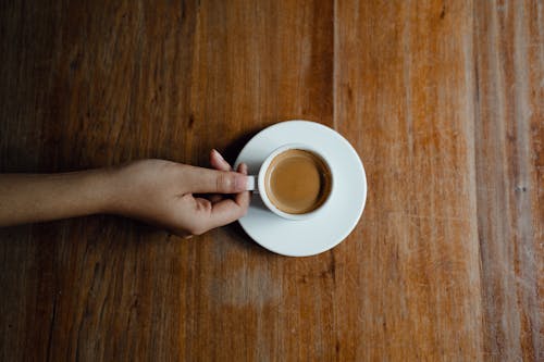 Crop person with cup of coffee at wooden table