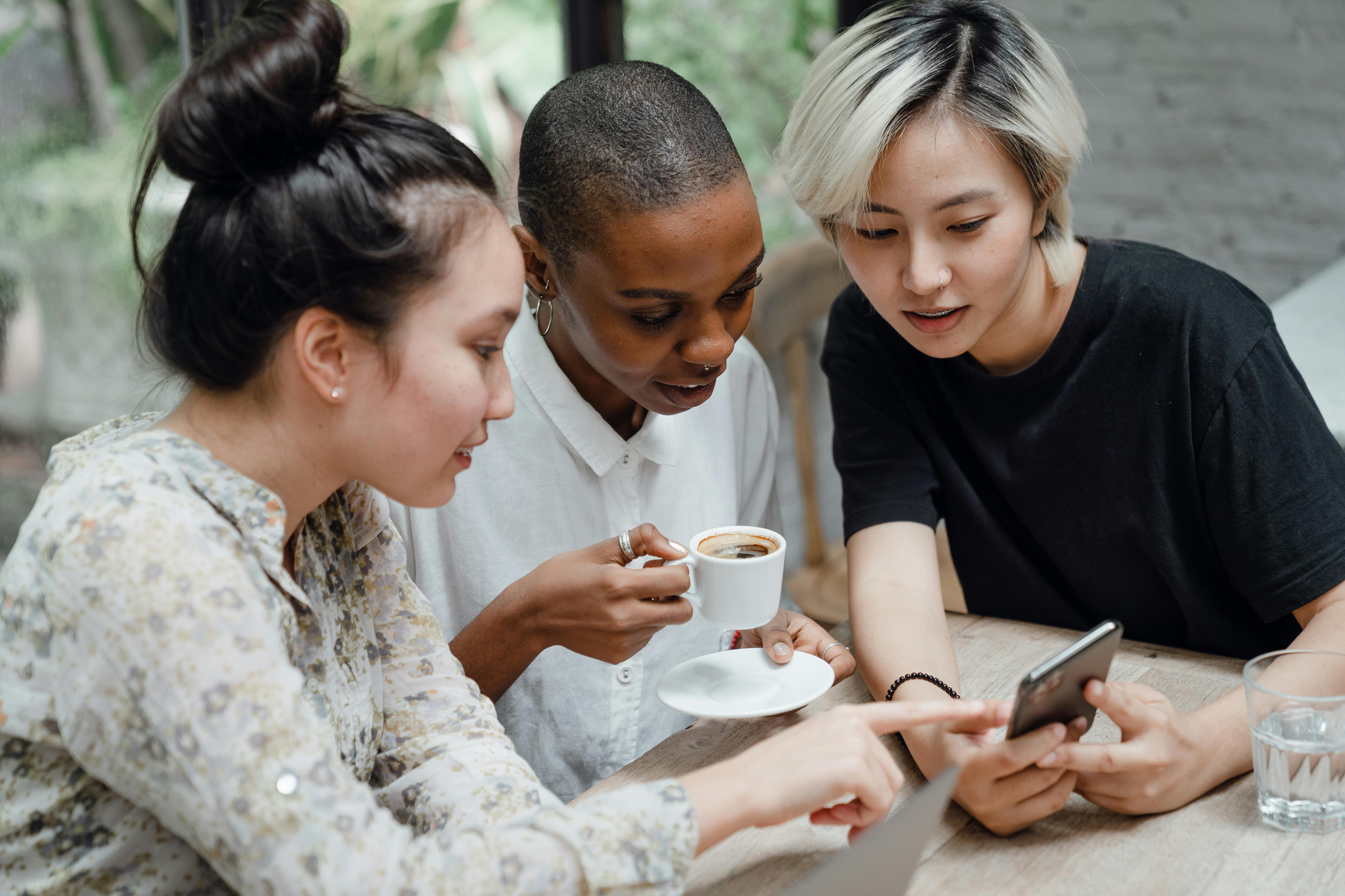 diverse female friends checking social media on mobile in cafe