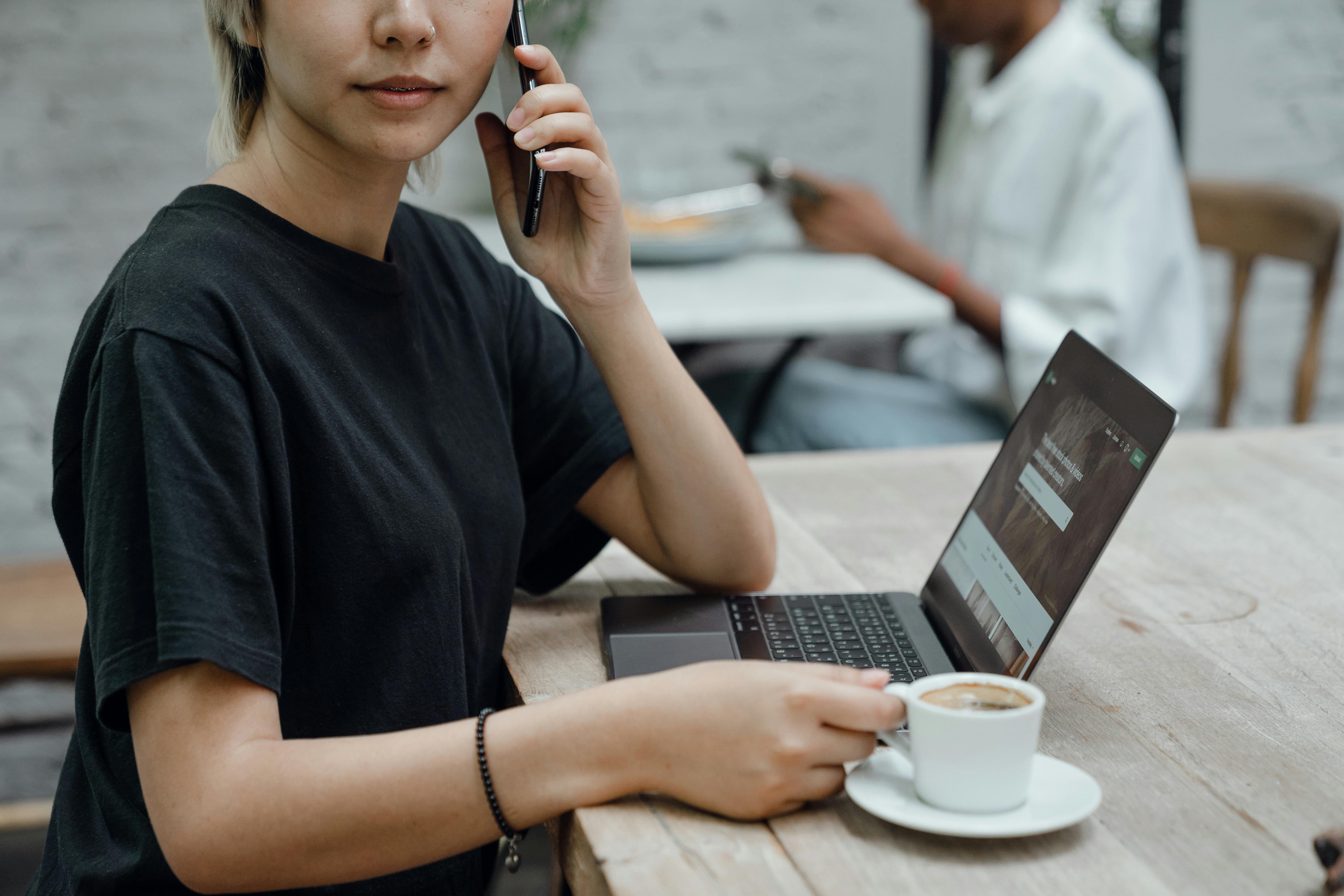 crop female talking on mobile phone with coffee and laptop