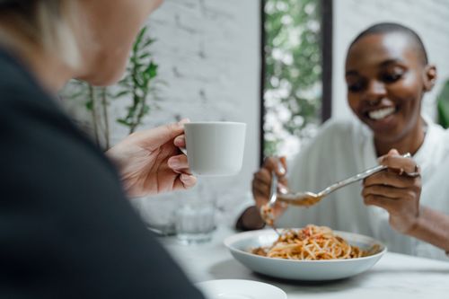 Free Positive young African American female enjoying time and talking with friend while having pasta in modern cafe Stock Photo