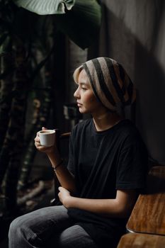一位年轻女子戴着无檐帽，身着休闲服装，在安静的咖啡馆里享用咖啡