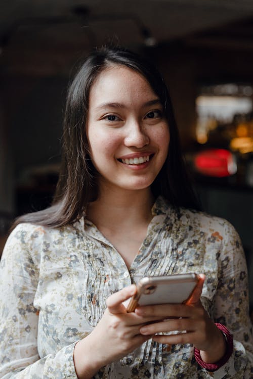 Young positive Asian woman using smartphone in cafe