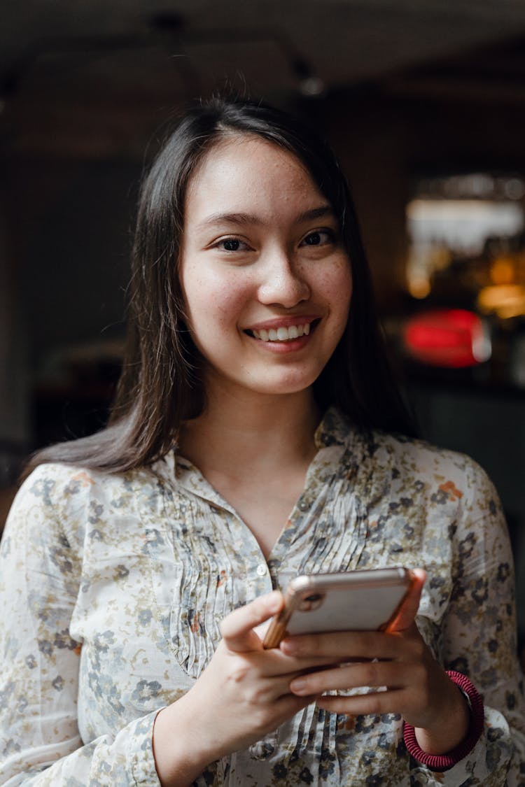 Young Positive Asian Woman Using Smartphone In Cafe