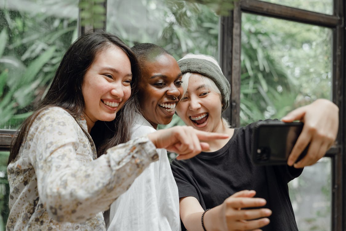 Cheerful diverse female friends laughing at just taken selfie