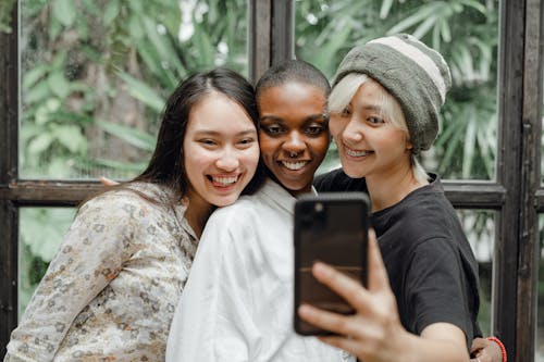 Free Cheerful young ladies hugging and taking selfie in modern cafe Stock Photo