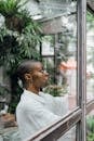 Through glass side view of young black female in modern outfit standing open mouthed near window in cafe and taking photo of interesting object on street with surprised face