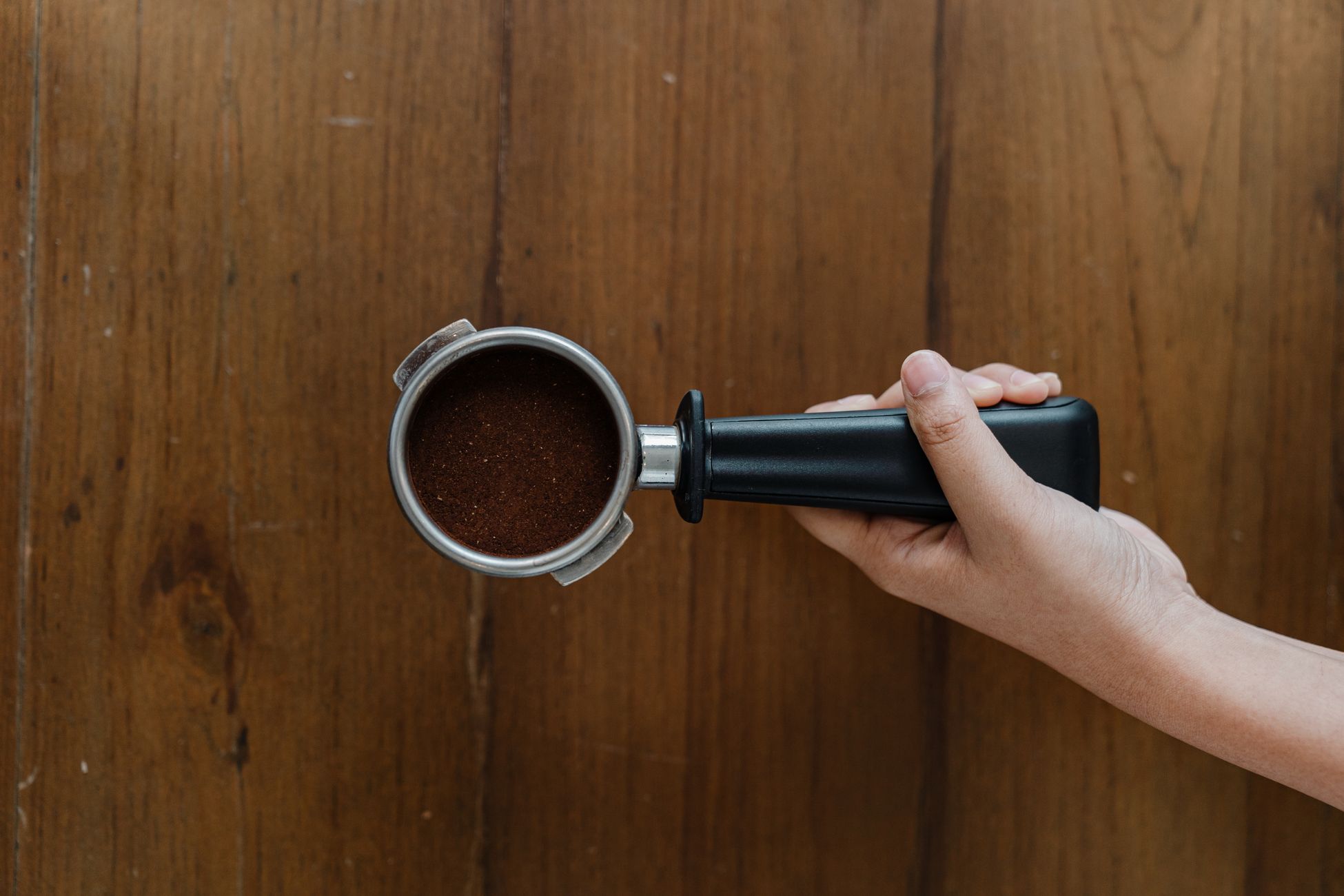 Top view of crop unrecognizable person placing group handle filled with freshly ground coffee on wooden table