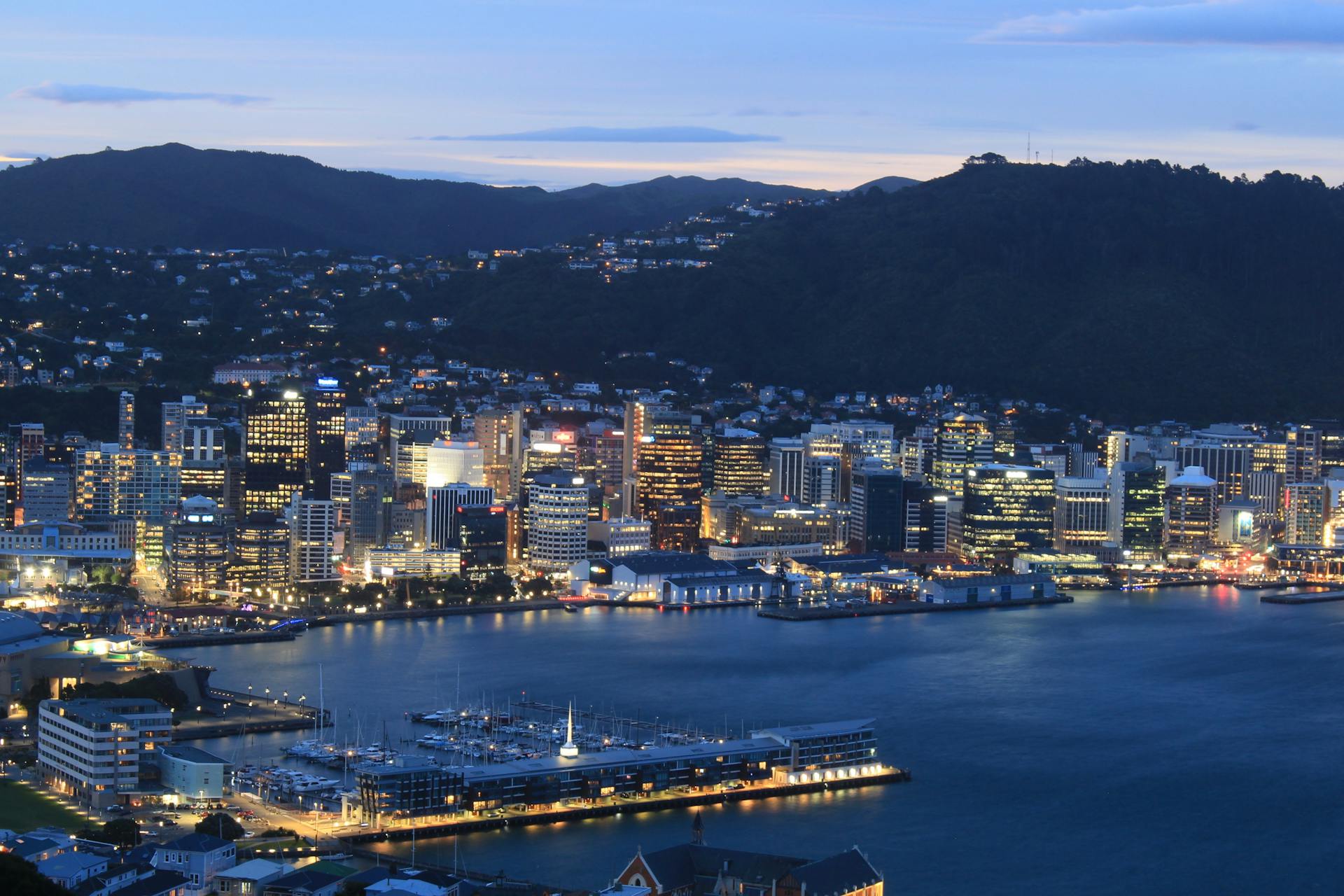 A striking evening aerial view of Wellington city skyline with vibrant lights reflecting on the waterfront.