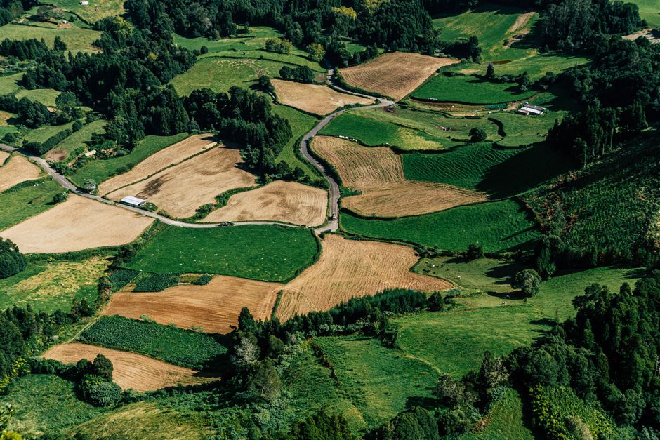 Impresionante vista aérea de diversos campos agrícolas con manchas verdes y marrones, ilustrando patrones de tierras rurales.