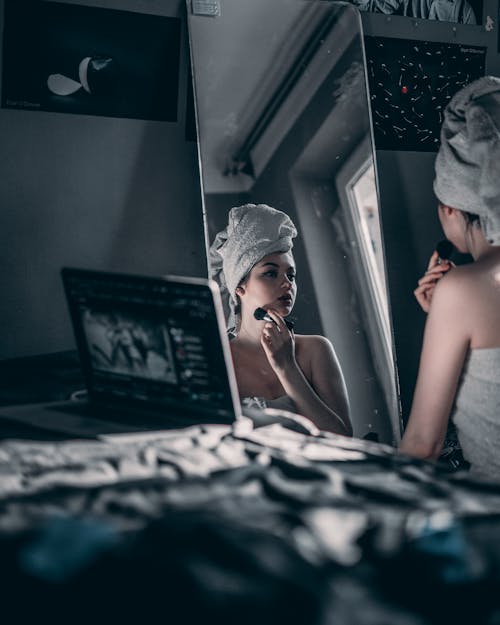 Woman reflecting in mirror while applying makeup