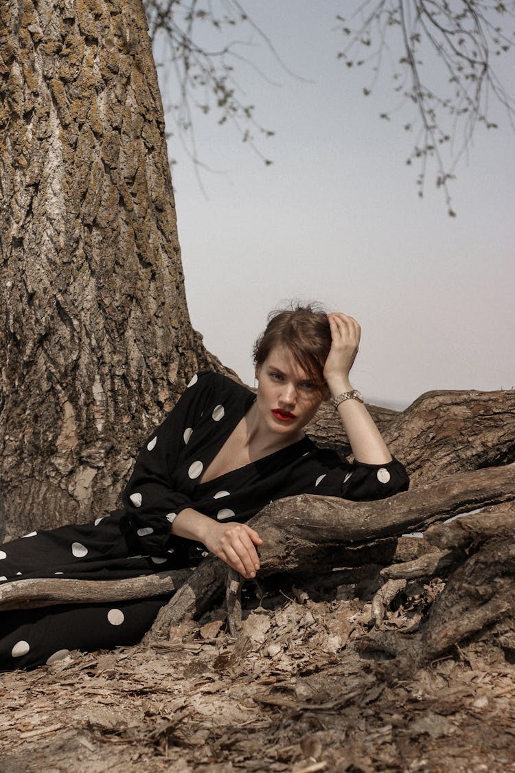 A Woman In A Polka Dot Dress Leaning On The Roots Of A Tree