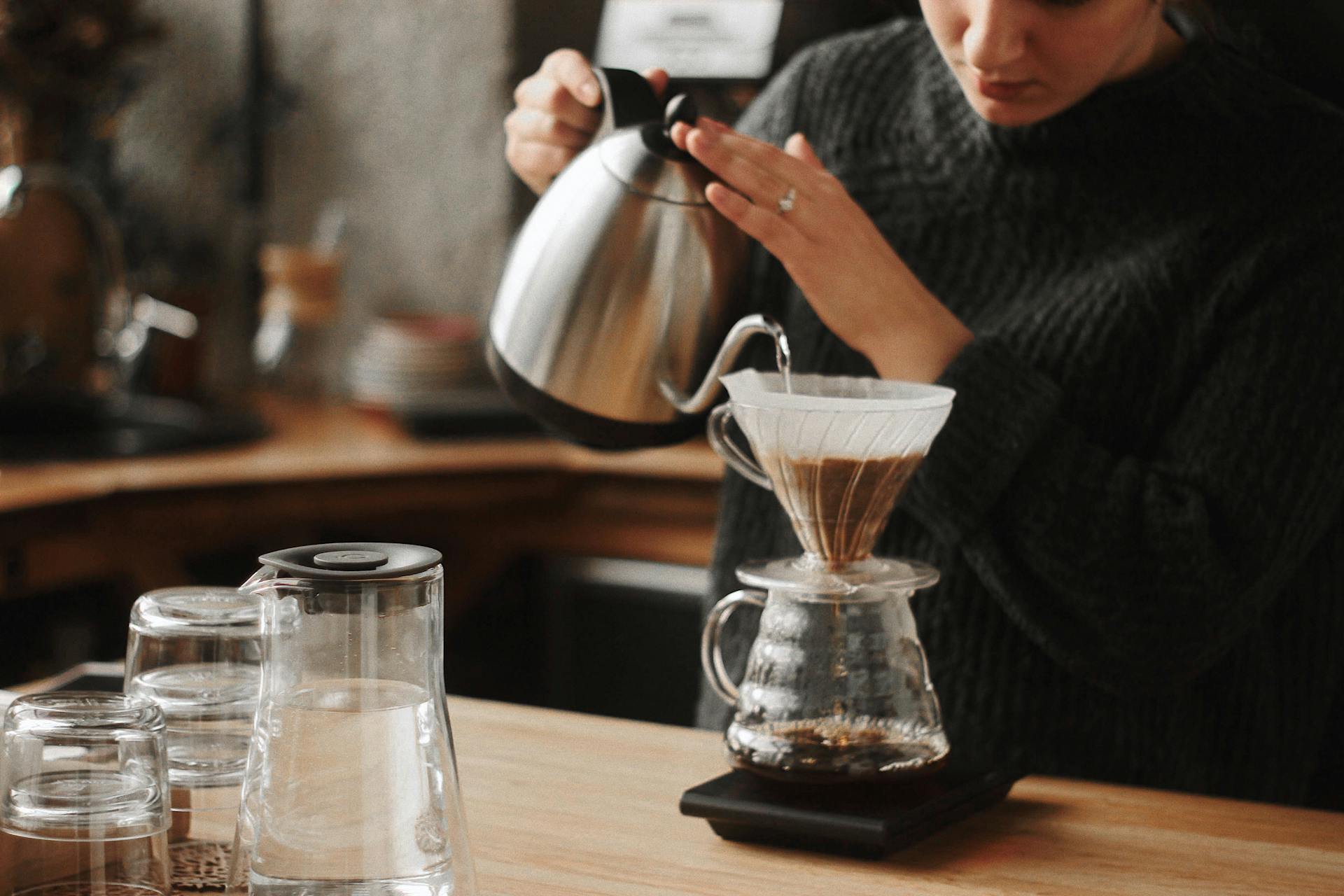 A woman pours hot water over a coffee dripper in a cozy café. Perfect morning ritual.