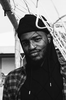Black and white of content masculine African American male in head wear and plaid shirt looking at camera near football goal net