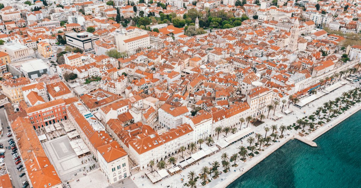 Amazing drone view of historical buildings with red tile roofs and modern promenade near turquoise sea in Split