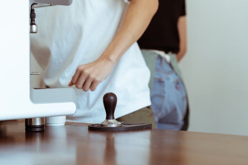 Crop cafe workers at table with coffeemaker and tamper