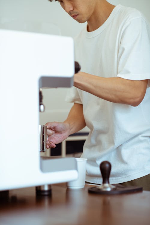 Crop cafe worker whipping milk using coffee machine