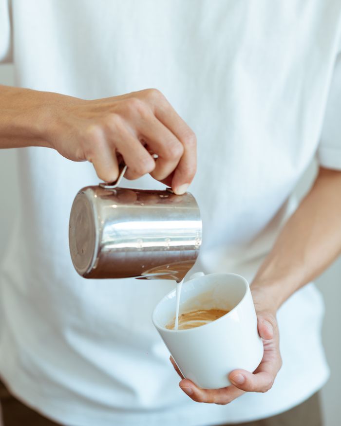 A barista pouring milk from a small jug into a white mug