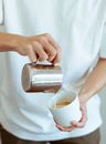 Crop barista pouring milk into mug