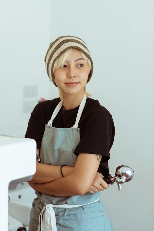 Glad barista with arms crossed near coffee machine