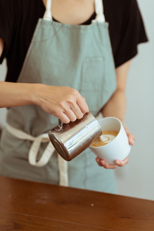 Free Crop barista pouring milk in cup with cappuccino Stock Photo