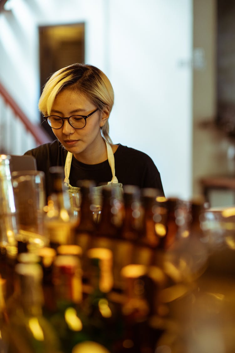 Content Woman In Black Shirt Behind Row Of Bottles