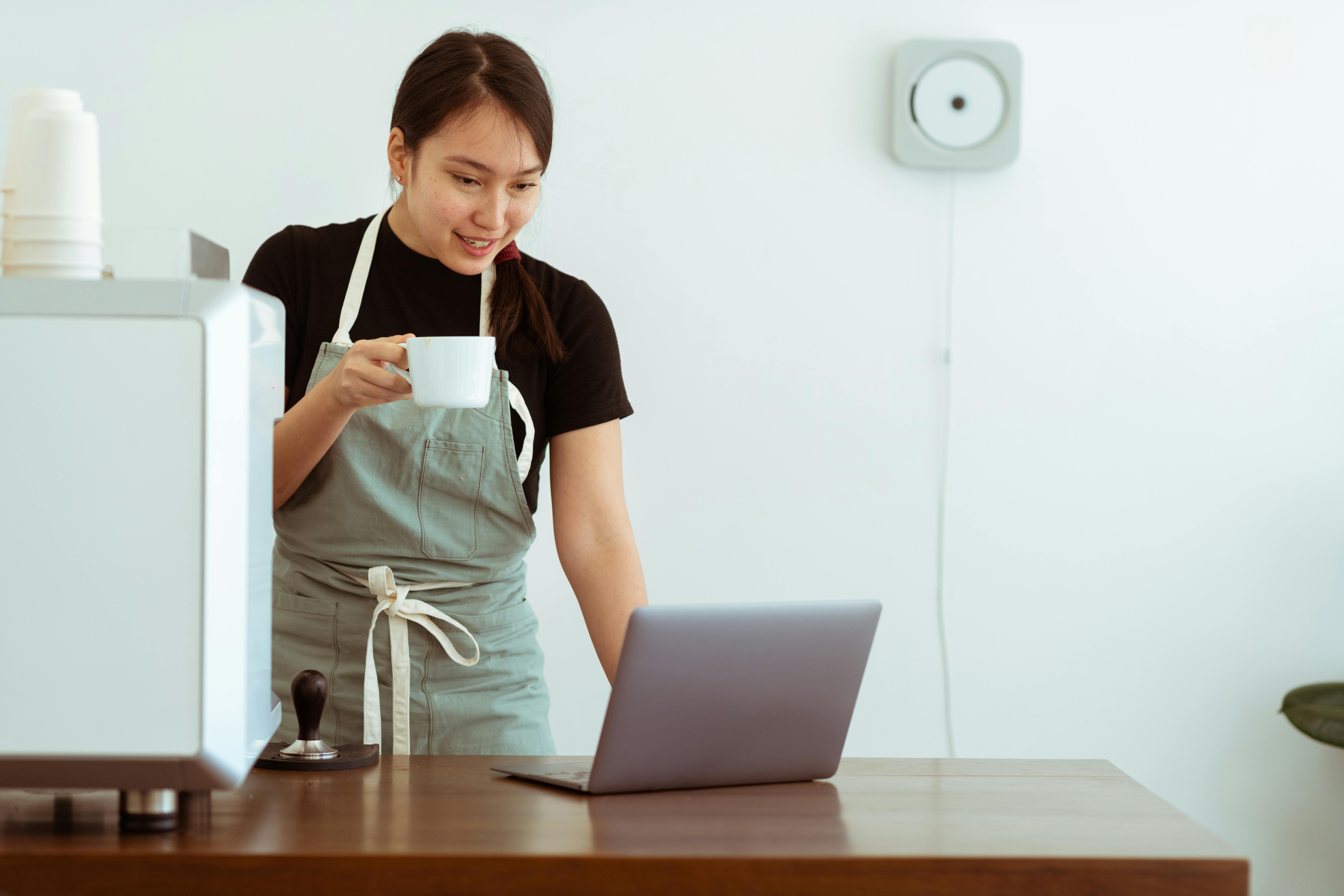 cheerful woman with cup of beverage working on laptop
